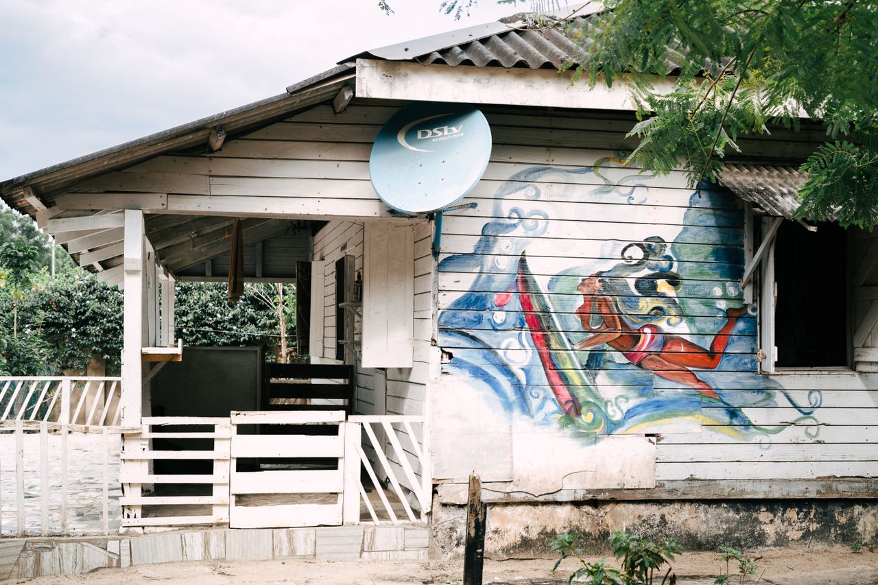 A rustic wooden house with vibrant street art mural and satellite dish.